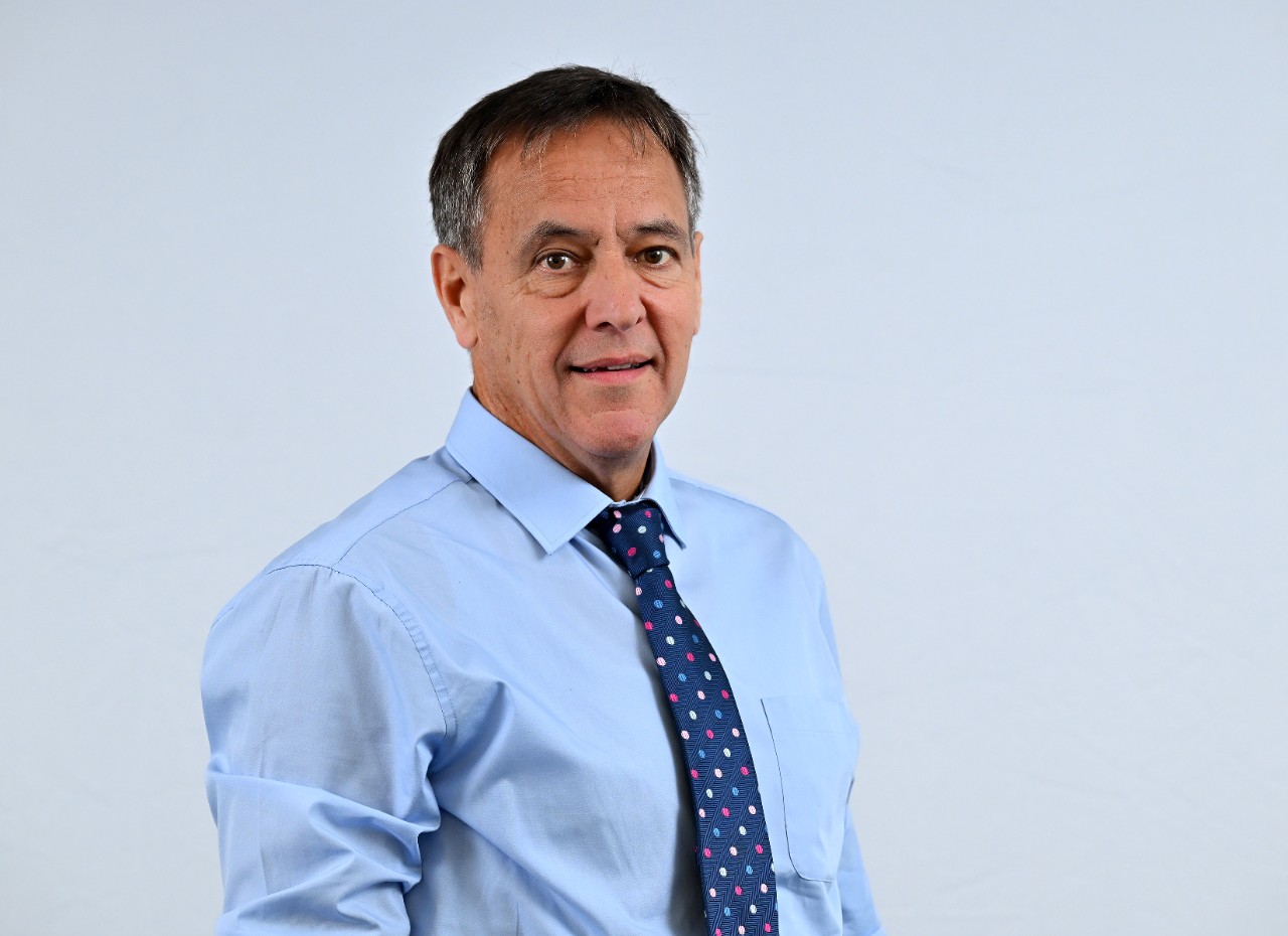 Cormac McKervey, white, late-middle aged male, short dark hair, greying at the sides, brown eyes, smiles, wearing a light blue shirt and brightly-spotted dark blue tie.