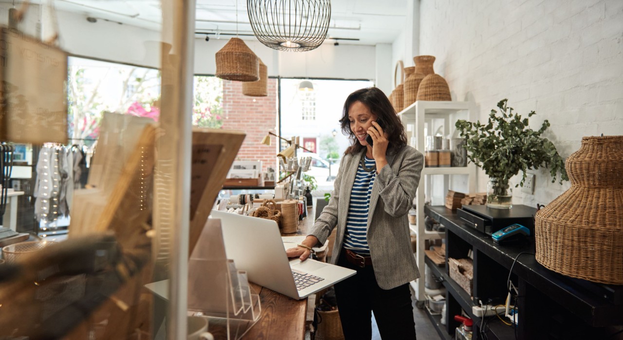 Woman in shop on phone looking at laptop