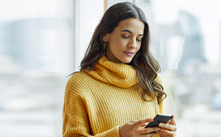 Person in a yellow sweater holding a smartphone indoors