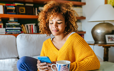 Person in a cozy living room holding a smartphone and a mug.