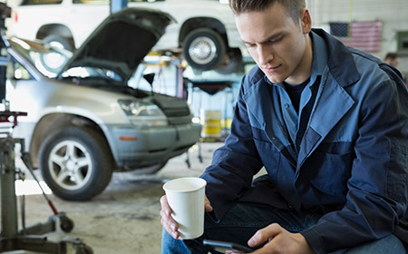 Photo of a car mechanic taking a break with coffee and phone