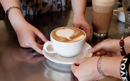 Photo of two pairs of hands holding a coffee cup and saucer