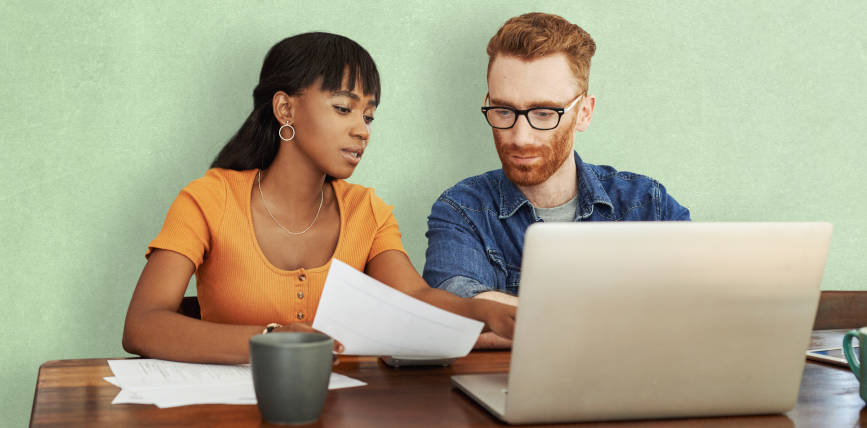 Image shows a woman and man sat at a table and working together in front of a laptop