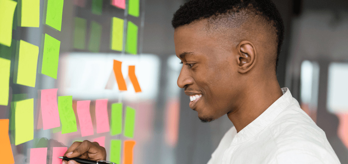 Photo of young businessman adding notes to a transparent display board