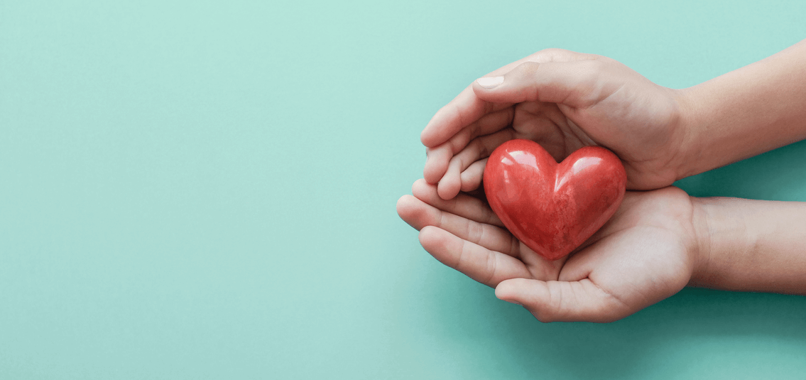 A pair of hands cupping a red love heart model