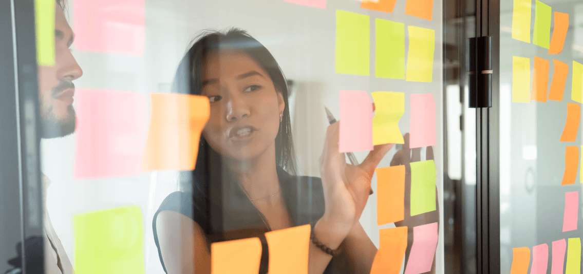 two people in office, planning using post-it notes on a glass partition