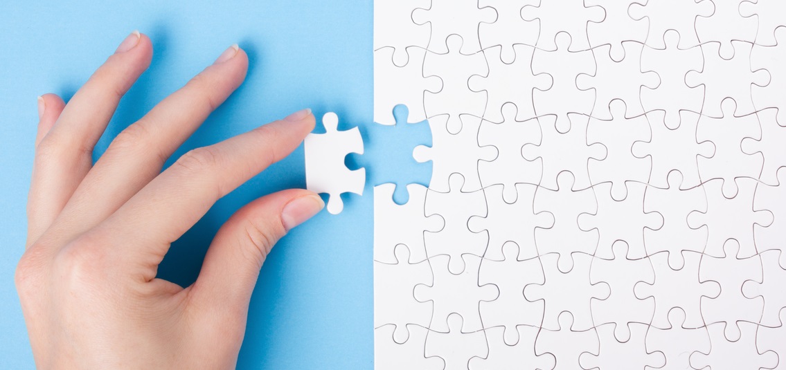 photo of a hand, putting the last piece into an all-white jigsaw