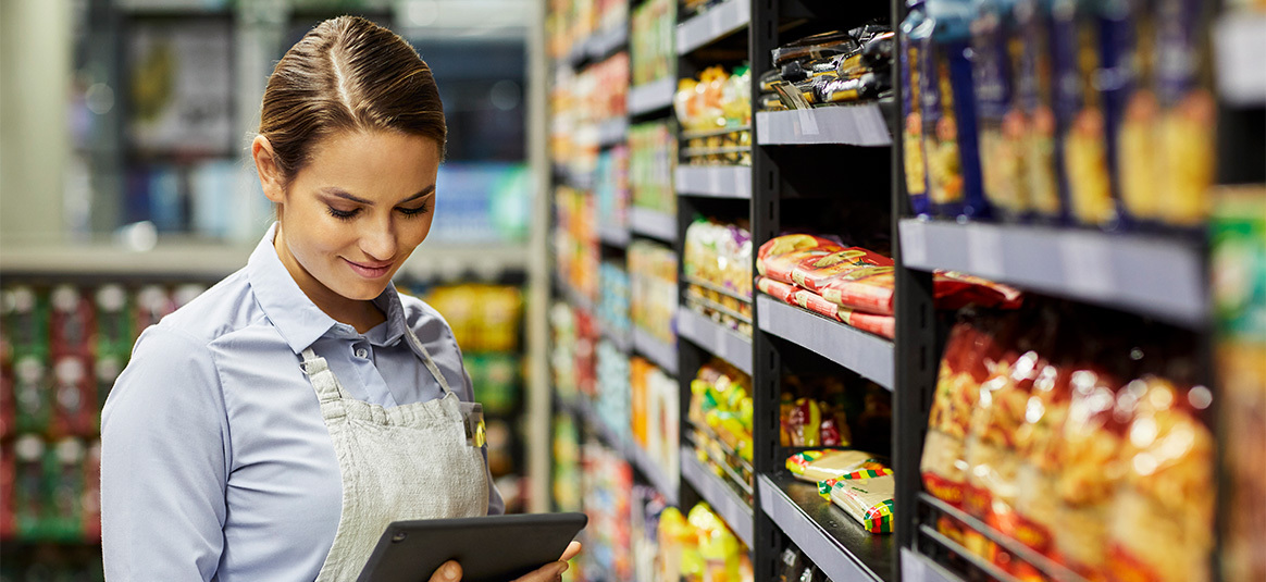 Woman smiling, looking at a tablet in a supermarket