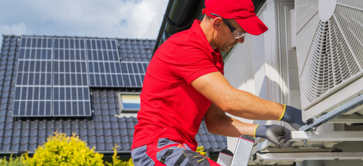 Photo of a workman instilling a heat pump to the exterior of a building.