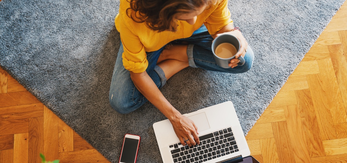 A woman sitting cross-legged on floor with laptop and coffee
