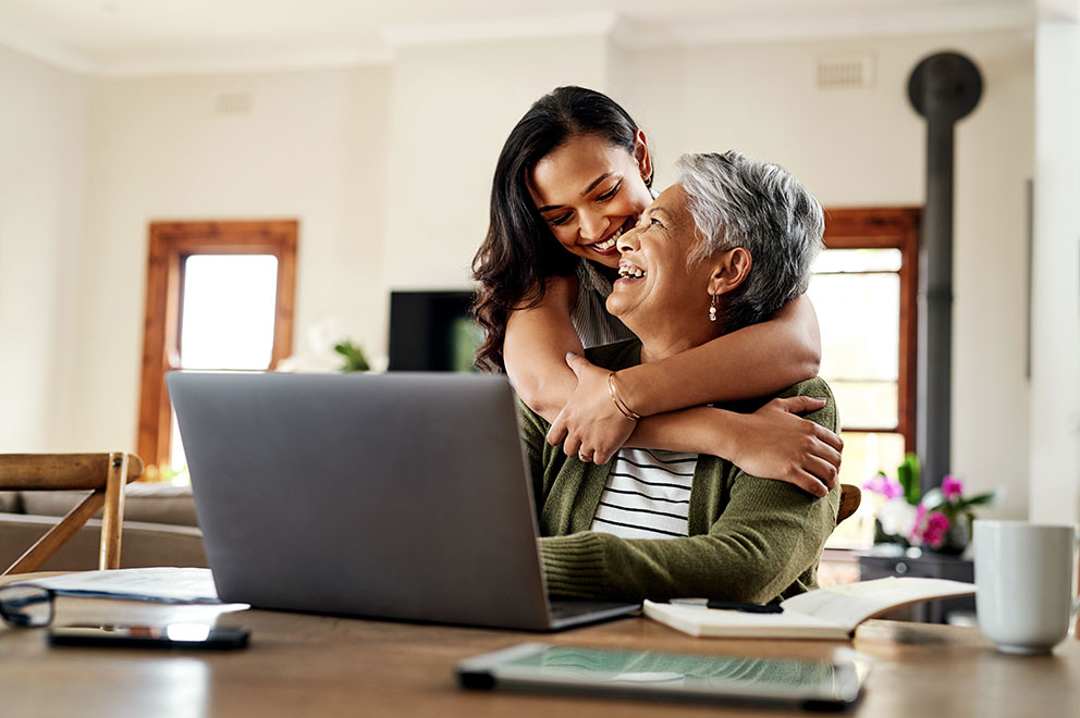 Mother and daughter hugging whilst sitting at laptop